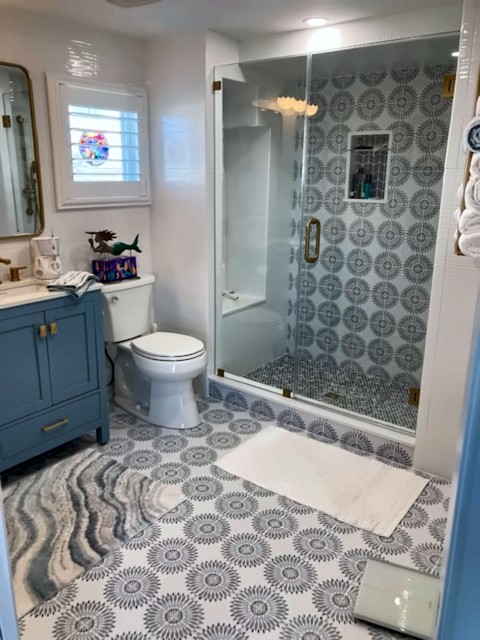 Bathroom with patterned tile floor, frameless glass shower and blue vanity