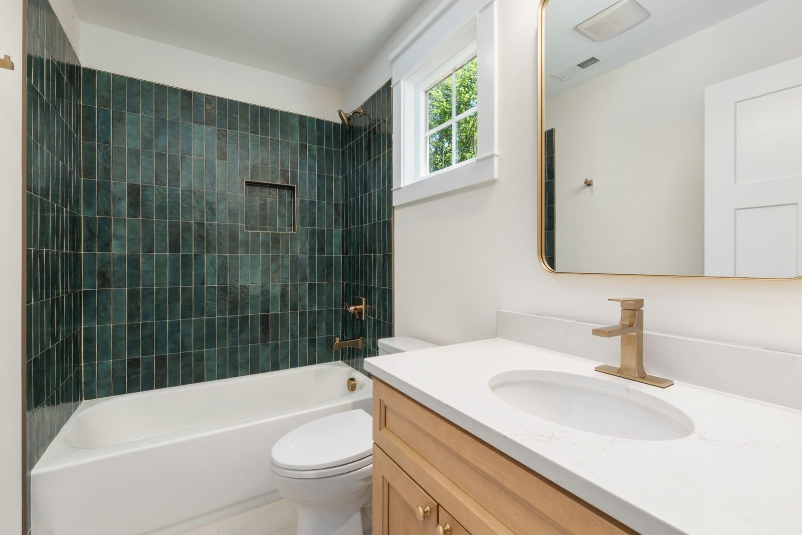 Bathroom with green tile wall, white tub and wood vanity