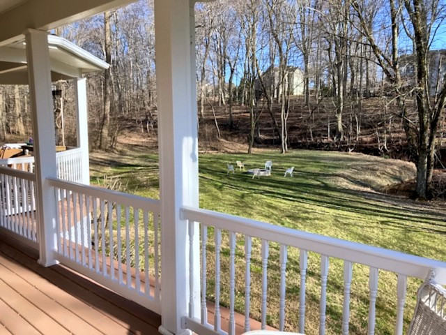 Covered porch with white railings overlooking a wooded lawn