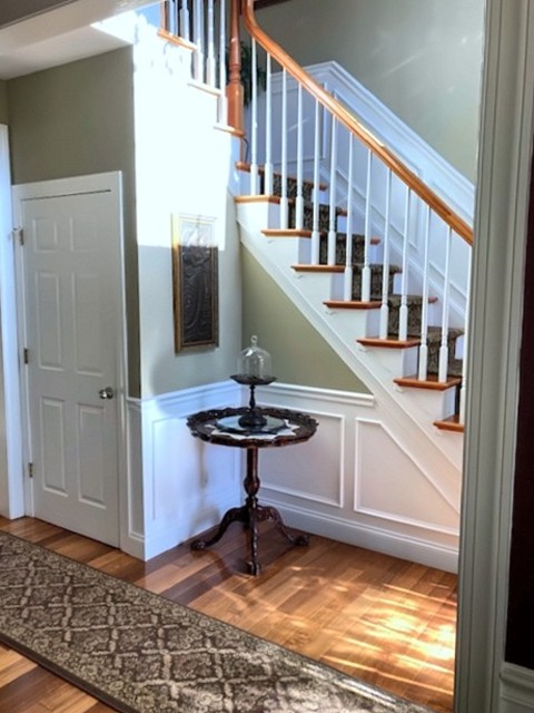 Foyer staircase with white balusters, wood rail and wainscoting