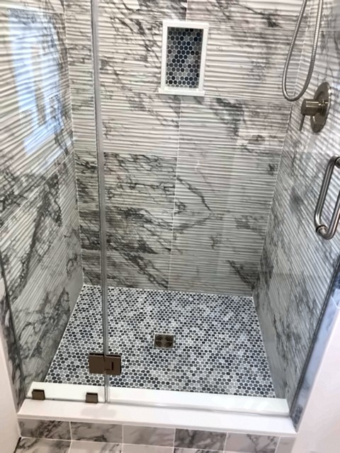 Glass-enclosed shower with marble-look wall tile and hex mosaic floor