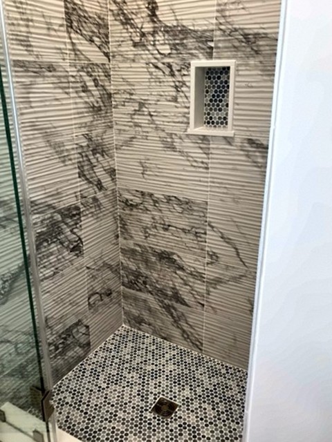 Marble-look tile shower with penny tile floor and mosaic niche