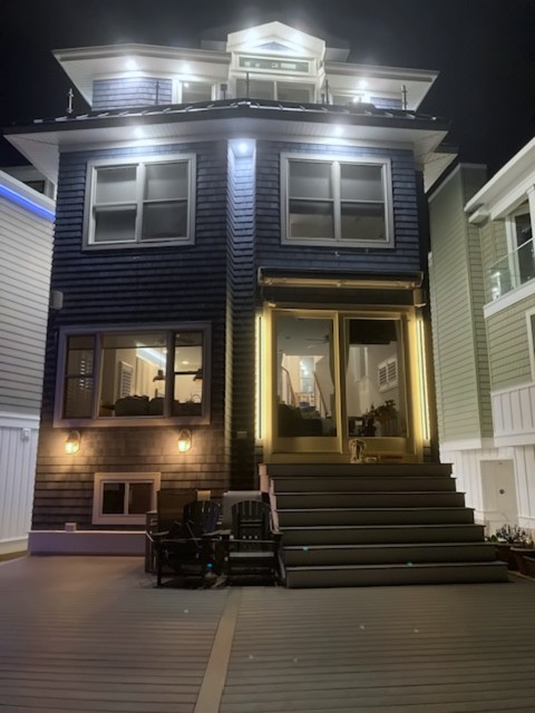 Two-story shore home with lit front entry and wide steps at night
