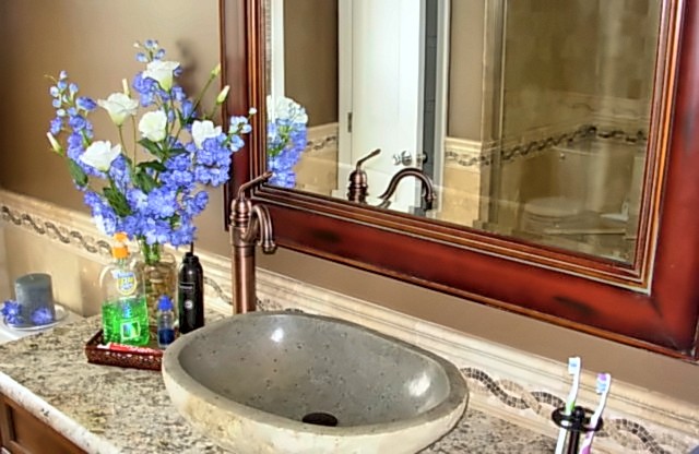 Portfolio photo: Stone vessel sink on a granite vanity with framed mirror