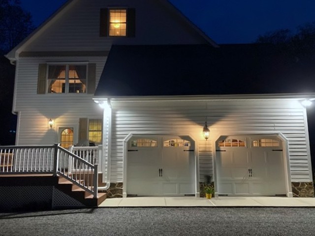 Two-car garage with carriage-style doors and deck stairs at dusk