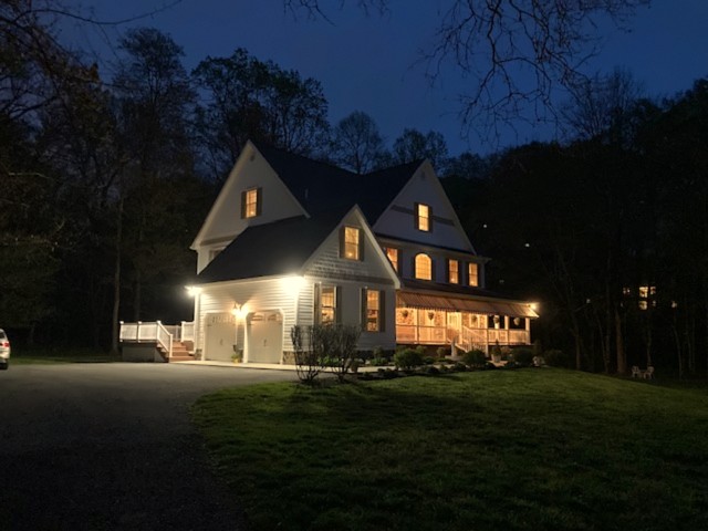 White farmhouse-style home with lit wraparound porch at dusk